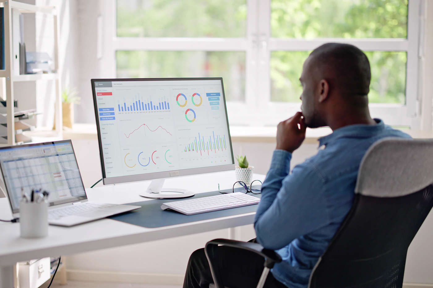 A man looking at data on a desktop and laptop.