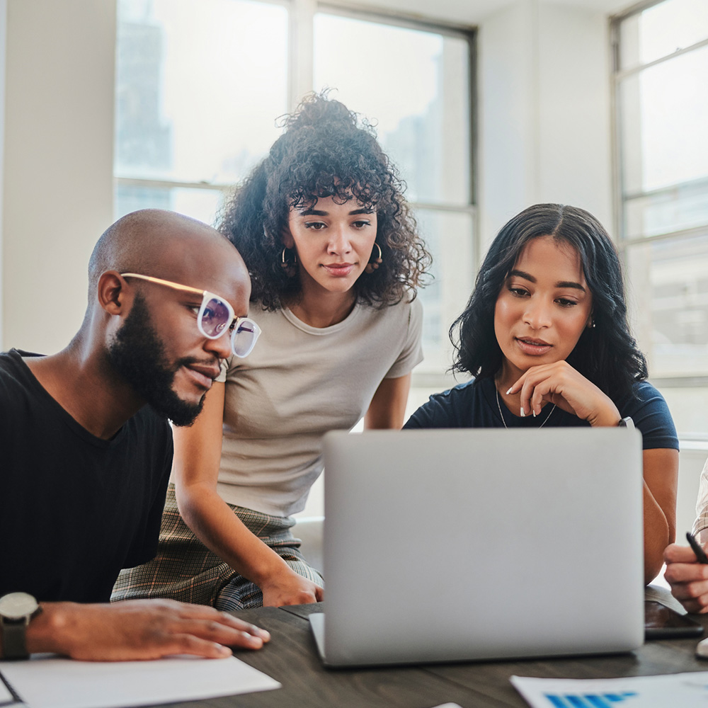 A male and two women coworkers looking at a laptop screen. 