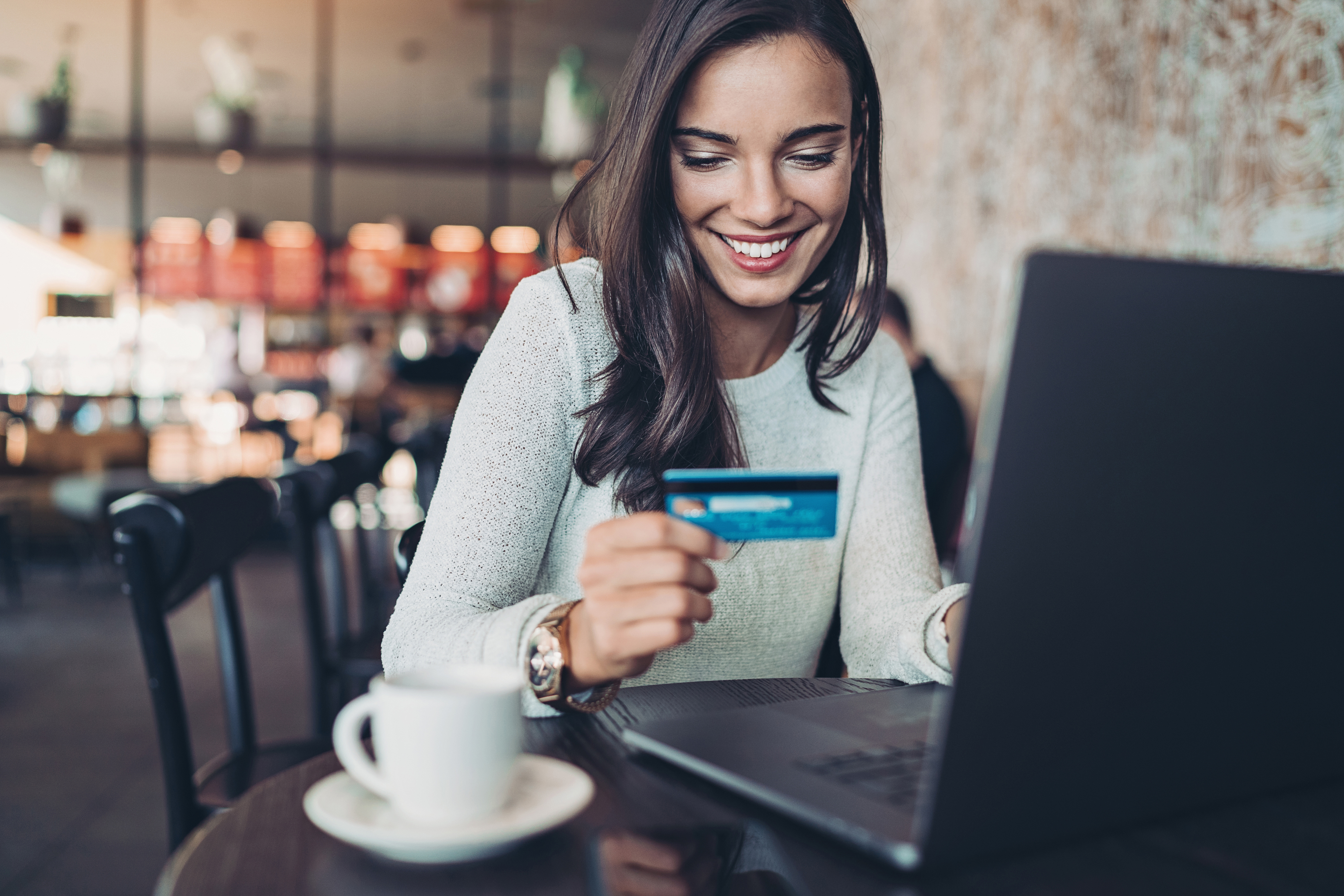 Smiling businesswoman holding a credit card and using laptop in a restaurant