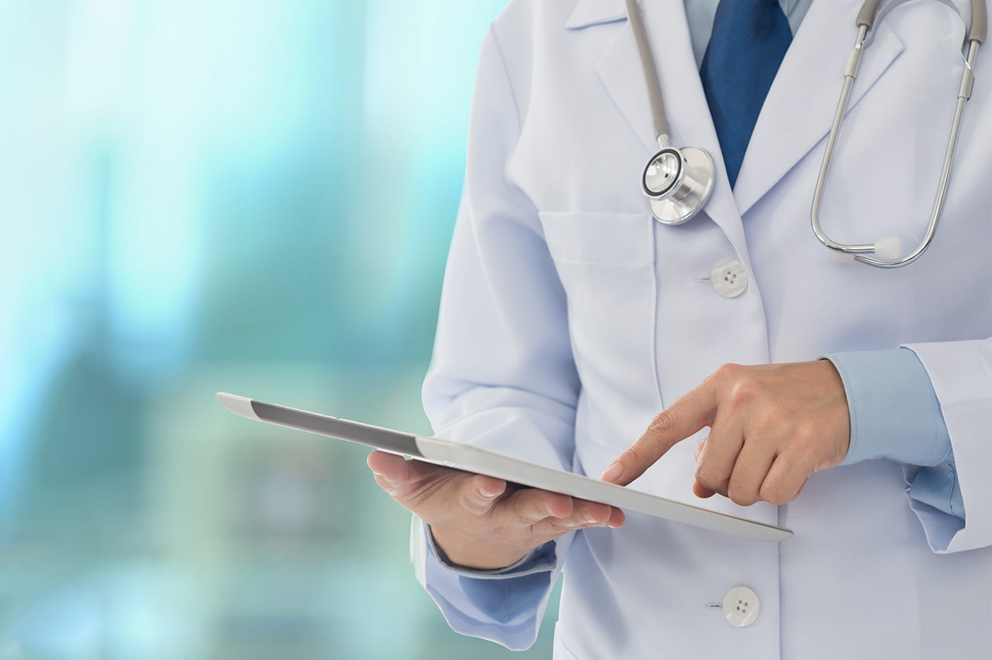 Man wearing a labcoat with a stethoscope around their neck working on an iPad.